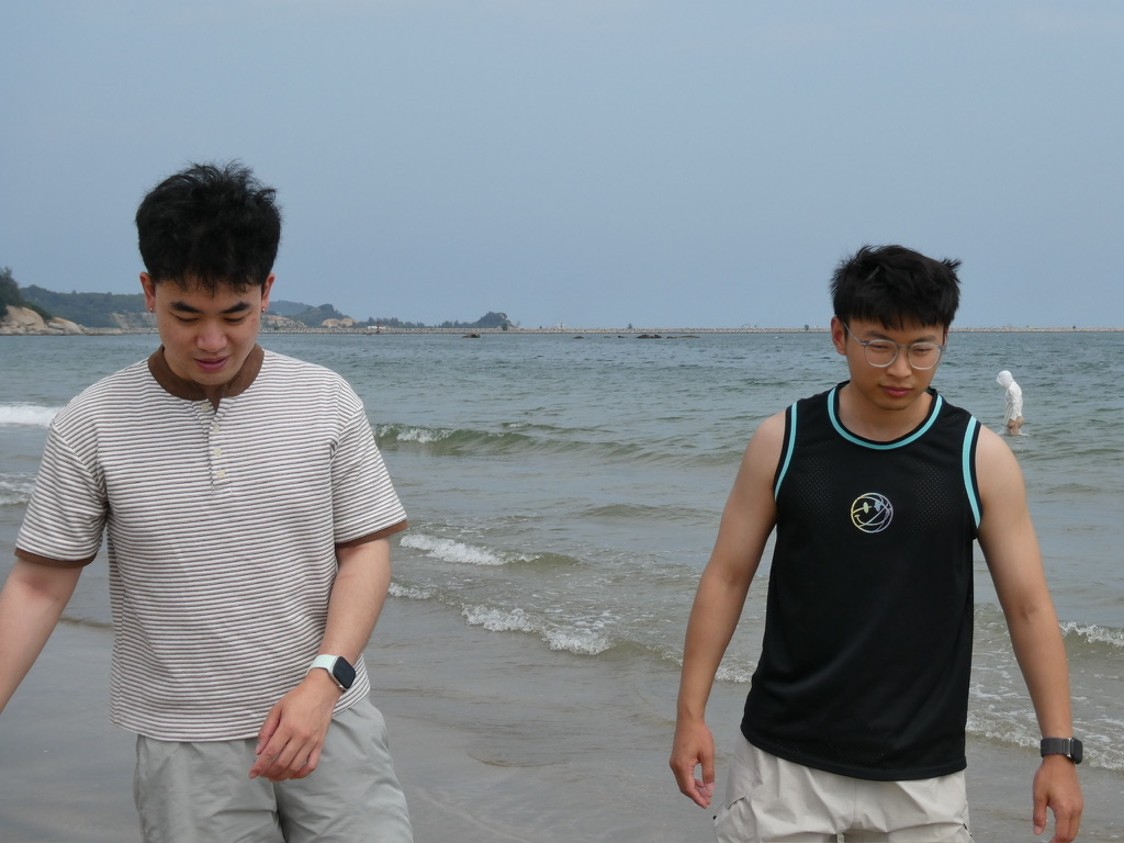 Two friends walk at the edge of a calm beach.