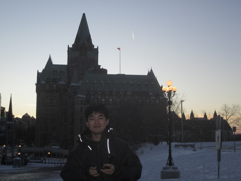 A person stands in front of a historic building and glowing street lamps in winter.