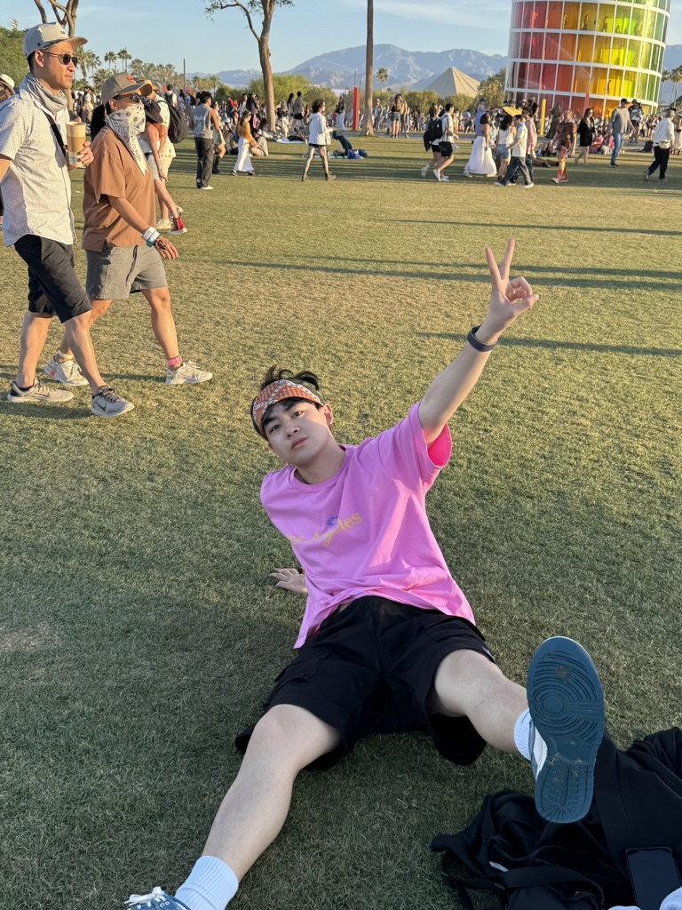 A person wearing a pink shirt raises a peace sign on a festival lawn.