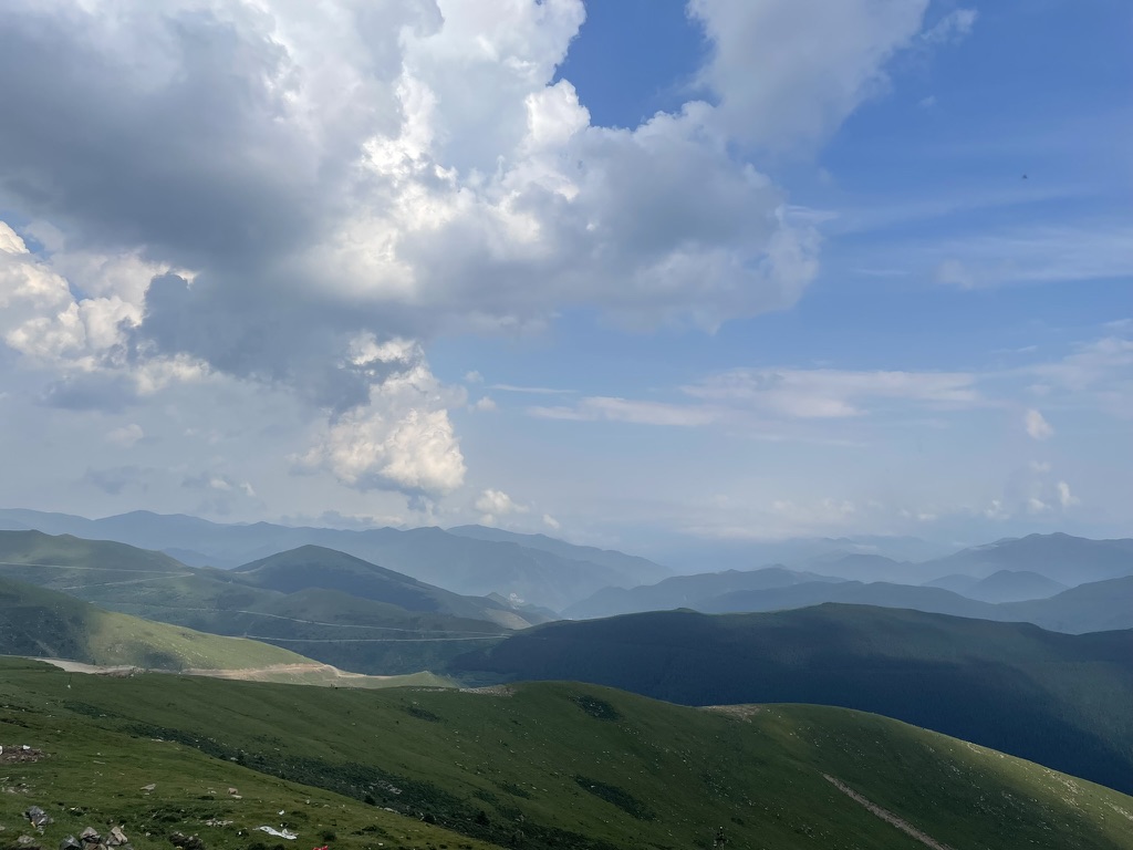 Layered green mountain ridges beneath a wide sky of bright and dark clouds.